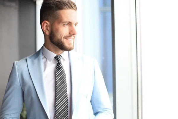 Hombre de negocios moderno en ropa formal de pie cerca de la ventana en la oficina — Foto de Stock