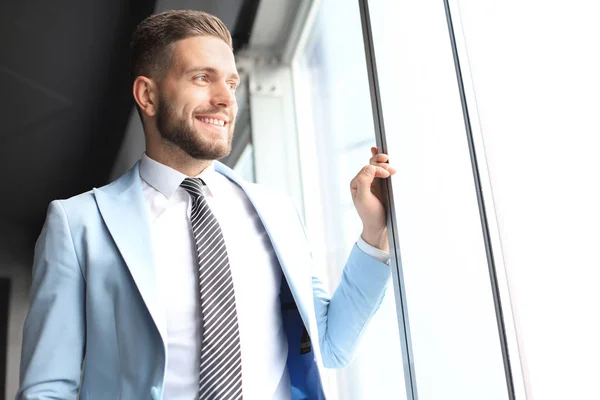 Hombre de negocios moderno en ropa formal de pie cerca de la ventana en la oficina —  Fotos de Stock