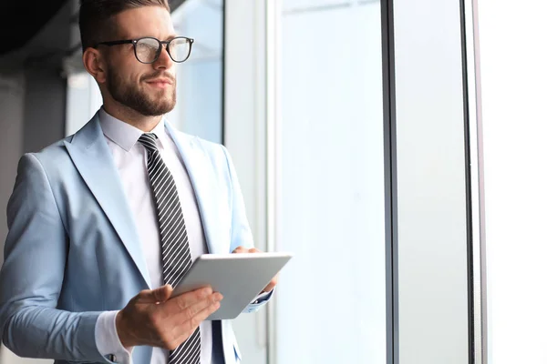 Moderne zakelijke man in formalwear met behulp van digitale Tablet terwijl staande in de buurt van venster in het kantoor — Stockfoto