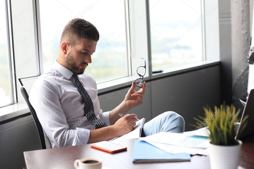 Focused modern businessman working and taking notes in his modern office