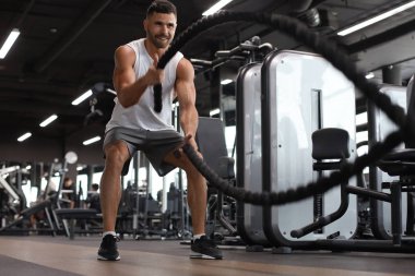 Savaş halatıyla atletik genç adam spor salonunda egzersiz yapıyor..