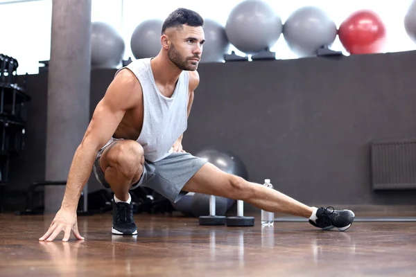 Człowiek na siłowni robi ćwiczenia rozciągające na podłodze. — Zdjęcie stockowe