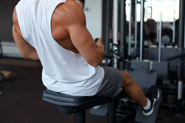 Fit i muskularny Człowiek za pomocą maszyny wiosłowe na siłowni. Widok z tyłu — Zdjęcie stockowe
