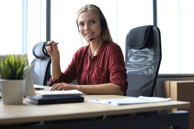 Kulaklıklı, güzel gülümseyen çağrı merkezi çalışanı modern ofiste çalışıyor.