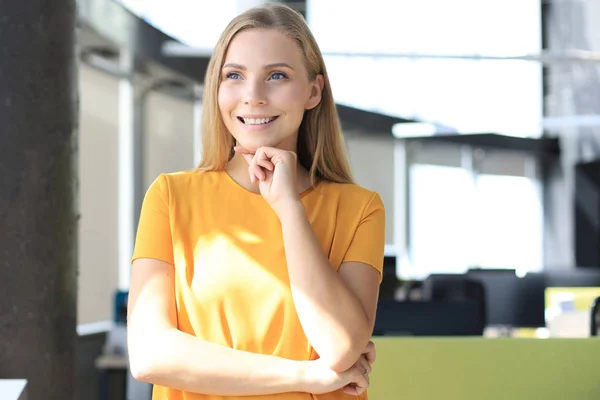 Atractiva mujer de negocios mirando a la cámara y sonriendo mientras está de pie en la oficina — Foto de Stock