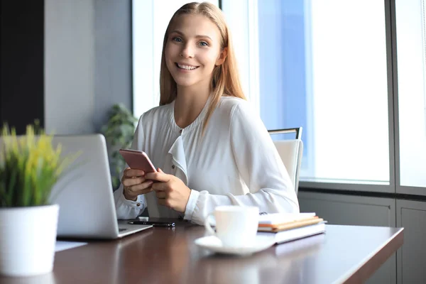 Krásná usměvavá obchodní žena sedí v kanceláři a dívá se do kamery — Stock fotografie