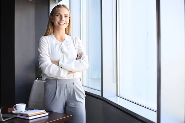 Atraktivní obchodní žena dívá na kameru a usmívá se, zatímco stojí v kanceláři — Stock fotografie