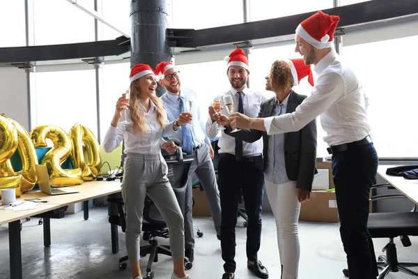 Business people are celebrating holiday in modern office drinking champagne and having fun in coworking. Merry Christmas and Happy New Year 2020.