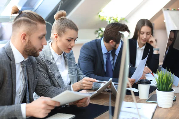 Groep jonge zakenmensen die werken, communiceren terwijl ze samen met collega's aan het bureau zitten. — Stockfoto