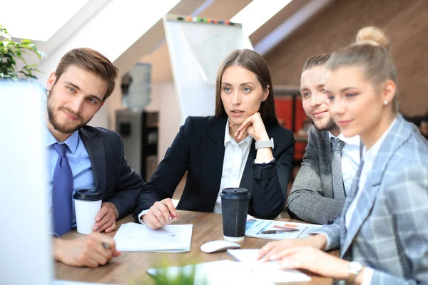 Gruppo di giovani imprenditori che lavorano, comunicano mentre sono seduti alla scrivania dell'ufficio insieme ai colleghi . — Foto Stock