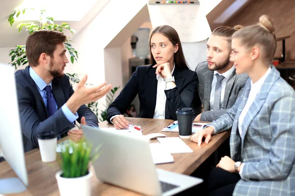 Gruppo di giovani imprenditori che lavorano, comunicano mentre sono seduti alla scrivania dell'ufficio insieme ai colleghi . — Foto Stock