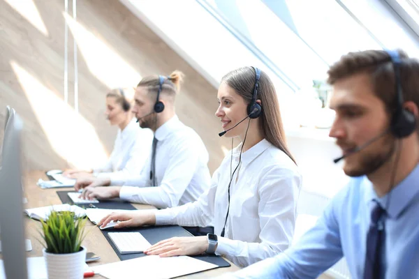 Operadora de atención al cliente femenina con auriculares y sonrisa acompañada por su equipo . —  Fotos de Stock