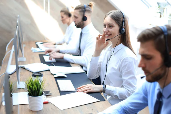 Operatore di assistenza clienti femminile con auricolare e sorridente accompagnato dal suo team . — Foto Stock