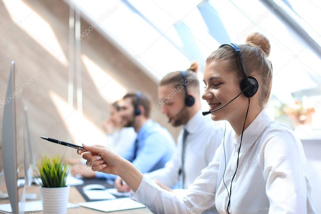 Female customer support operator with headset and smiling accompanied by her team.