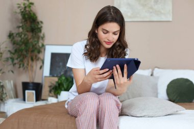 Çekici kadın yatakta oturuyor ve tabletini kullanıyor..