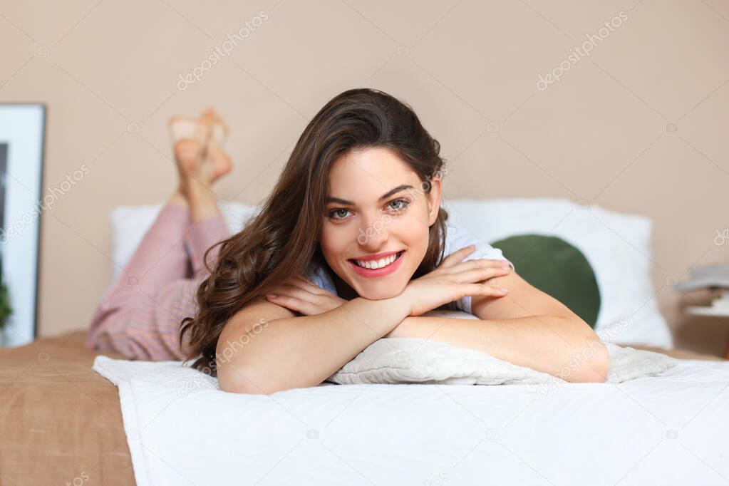 Cheerful woman on bed is smiling and looking at camera.