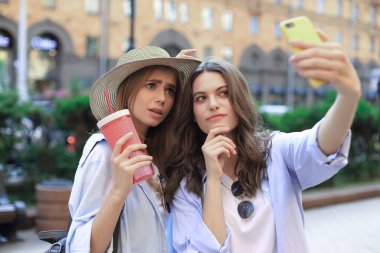 İki gülen arkadaş hafta sonunun tadını çıkarıyor ve şehrin arka planında selfie çekiyorlar..