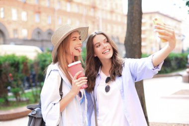 İki gülen arkadaş hafta sonunun tadını çıkarıyor ve şehrin arka planında selfie çekiyorlar..