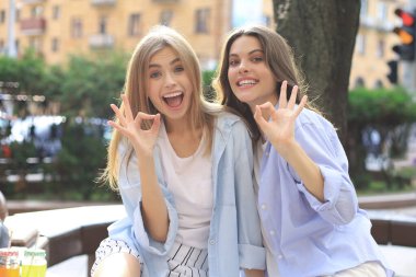 Sokakta poz veren iki genç gülümseyen hippi kadın. Olumlu yüz ifadeleri sergiliyor..