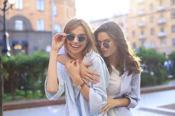 Dos hermosas chicas sonrientes en ropa de verano de moda posando en el fondo de la calle. Modelos se están divirtiendo y abrazando . —  Fotos de Stock