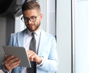 Ofiste pencerenin yanında dururken dijital tablet kullanarak formalwear modern iş adamı