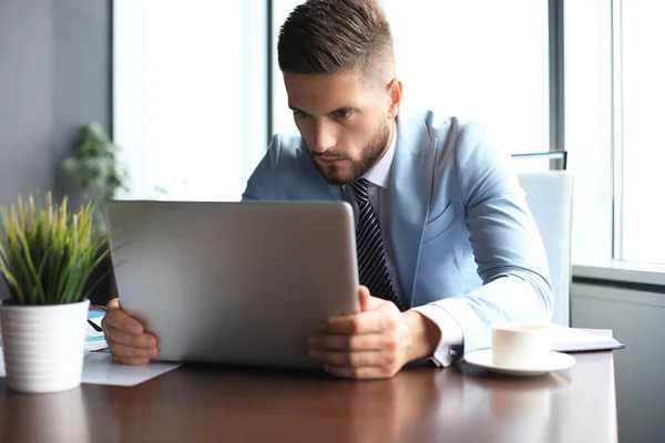 Goed uitziende zakelijke man houdt laptop terwijl zittend in het kantoor — Stockfoto