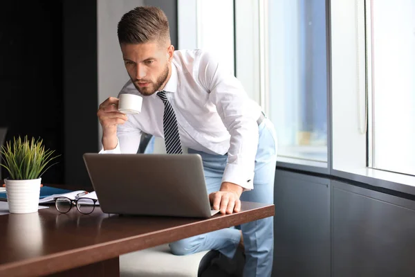 Przemyślany młody człowiek biznesu używa komputera i pije kawę podczas pracy w biurze — Zdjęcie stockowe