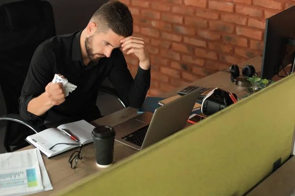 Ο κουρασμένος νεαρός δουλεύει με χαρτιά ενώ κάθεται στο γραφείο. — Φωτογραφία Αρχείου