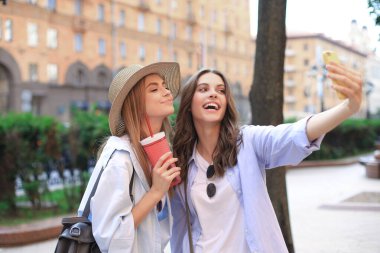 İki gülen arkadaş hafta sonunun tadını çıkarıyor ve şehrin arka planında selfie çekiyorlar..
