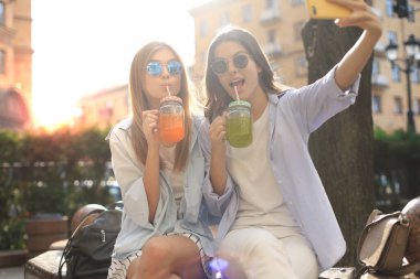 İki gülen arkadaş hafta sonunun tadını çıkarıyor ve şehrin arka planında selfie çekiyorlar..