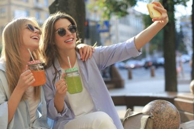İki gülen arkadaş hafta sonunun tadını çıkarıyor ve şehrin arka planında selfie çekiyorlar..