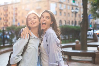 Sokakta poz veren iki genç gülümseyen hippi kadın. Olumlu yüz ifadeleri sergiliyor..