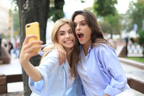 Dva smějící se přátelé užívají víkend spolu a dělat selfie na pozadí města. — Stock fotografie