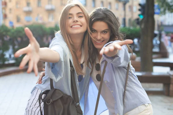 Dwie młode uśmiechnięte hipsterki w letnich ciuchach pozujące na ulicy.Kobieta wykazująca pozytywne emocje na twarzy. — Zdjęcie stockowe