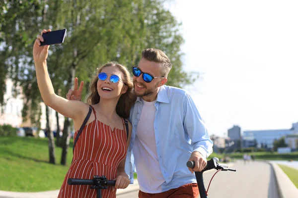 Preciosa pareja divirtiéndose conduciendo scooter eléctrico por la ciudad, teniendo un descanso, tomando selfie — Foto de Stock