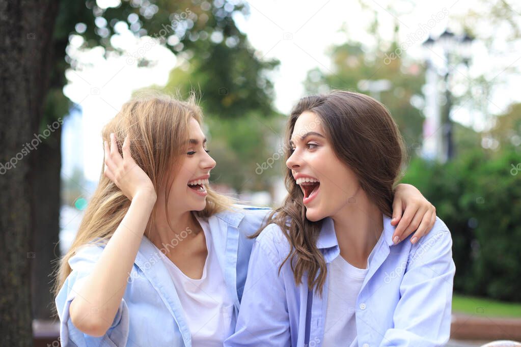 Two young smiling hipster women in summer clothes posing on street.Female showing positive face emotions.