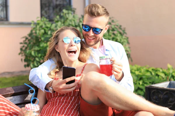 Romántica pareja joven en ropa de verano sonriendo y tomando selfie mientras se sienta en el banco en la calle de la ciudad — Foto de Stock