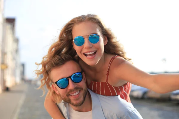 Guapo joven hombre llevando joven atractiva mujer en hombros mientras pasar tiempo juntos al aire libre — Foto de Stock