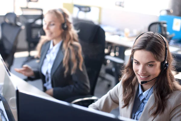 Operatore di assistenza clienti femminile con auricolare e sorridente, con collegi sullo sfondo. — Foto Stock