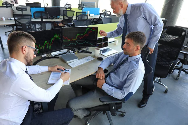 Grupo de hombres de negocios modernos en ropa formal que analizan los datos del mercado de valores mientras trabajan en la oficina . — Foto de Stock