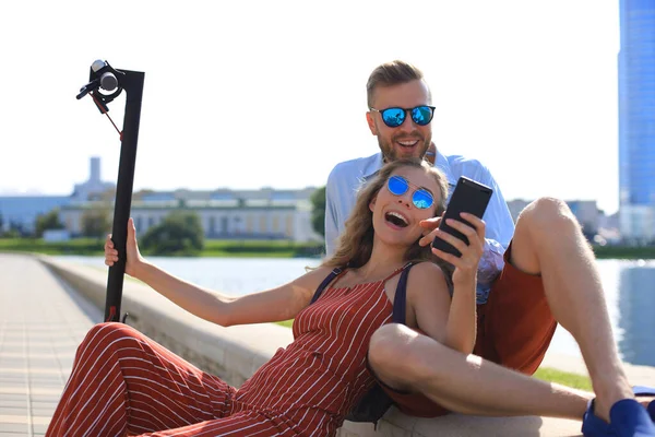 Kedves pár szórakozás vezetés elektromos robogó, egy kis szünetet vezetés, ül a folyóparton, selfie — Stock Fotó