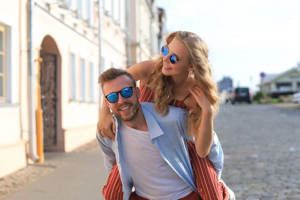 Guapo joven hombre llevando joven atractiva mujer en hombros mientras pasar tiempo juntos al aire libre —  Fotos de Stock