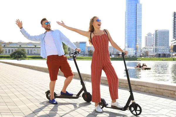 Preciosa pareja que se divierten conduciendo scooter eléctrico a lo largo del paseo marítimo de la ciudad —  Fotos de Stock