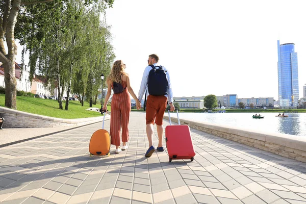 Vista traseira do casal turístico de mãos dadas e bagagem arrastando, visitando a rua, ao ar livre — Fotografia de Stock