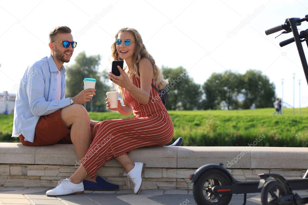 Lovely couple having fun driving electric scooter through the city, having a break, drinking coffee