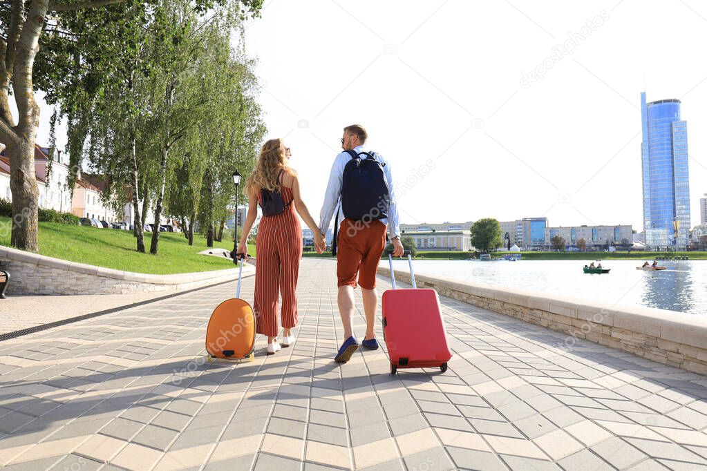 Rear view of tourist couple holding hands and dragging luggage, sightseeing visiting street, outdoors