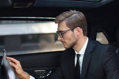 Düşünceli genç işadamı lüks arabada oturan ve tabletini kullanarak.