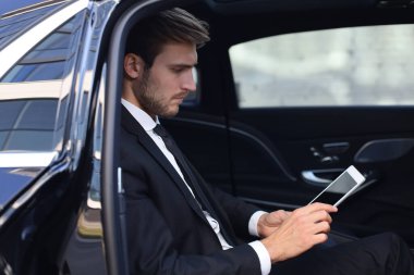 Düşünceli genç işadamı lüks arabada oturan ve tabletini kullanarak.