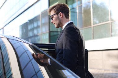 Zarif genç işadamı dışarıda dururken arabasına giriyor.