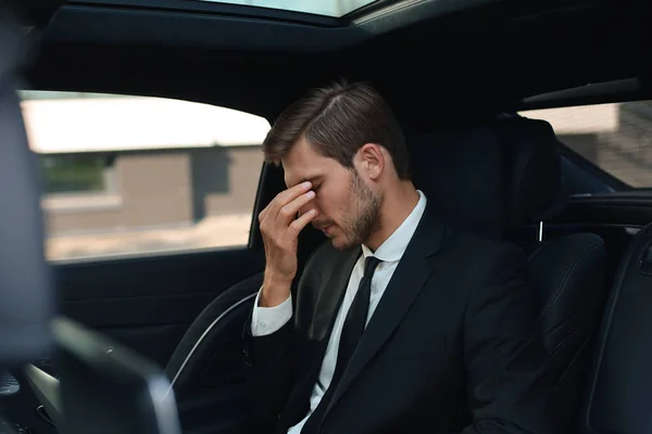 Cansado empresario sobrecargado de trabajo vestido con traje completo masajeando la nariz mientras está sentado en el coche . —  Fotos de Stock